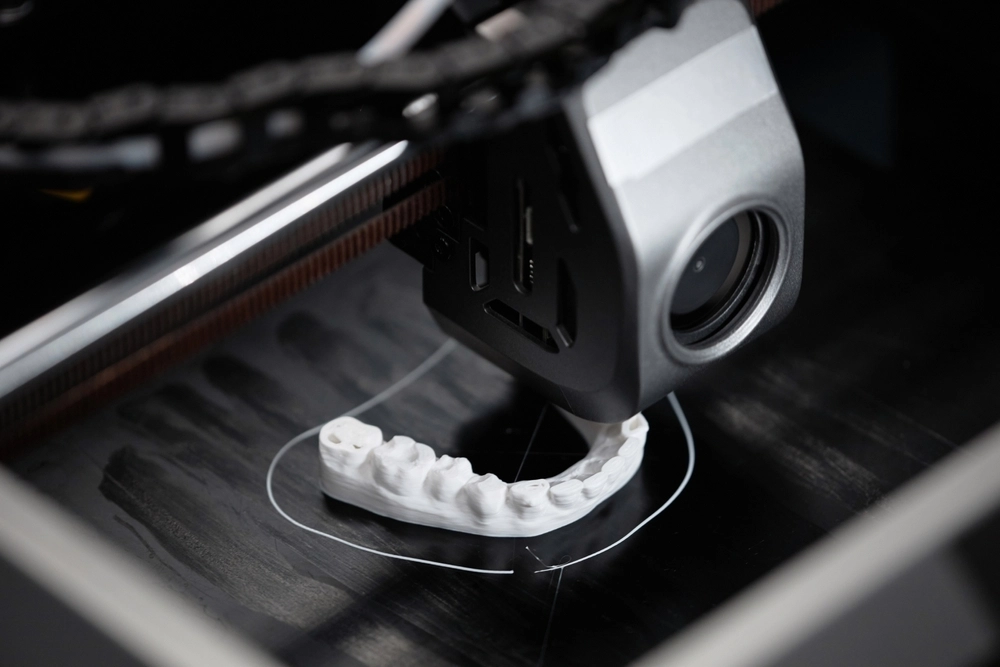 Der 3D-Drucker produziert einen Zahn, der sich zentral in der Maschine befindet.